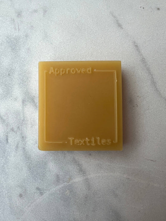 25g block of hand-poured beeswax stamped with the Approved Textiles mark, sourced from Huff's Honey Farm in Trout Run, Pennsylvania.