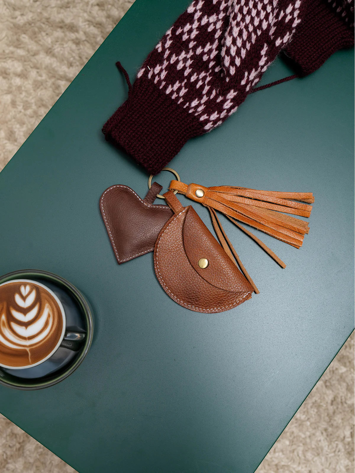 Brown leather pouch with tassels on a green surface next to a cup of coffee.