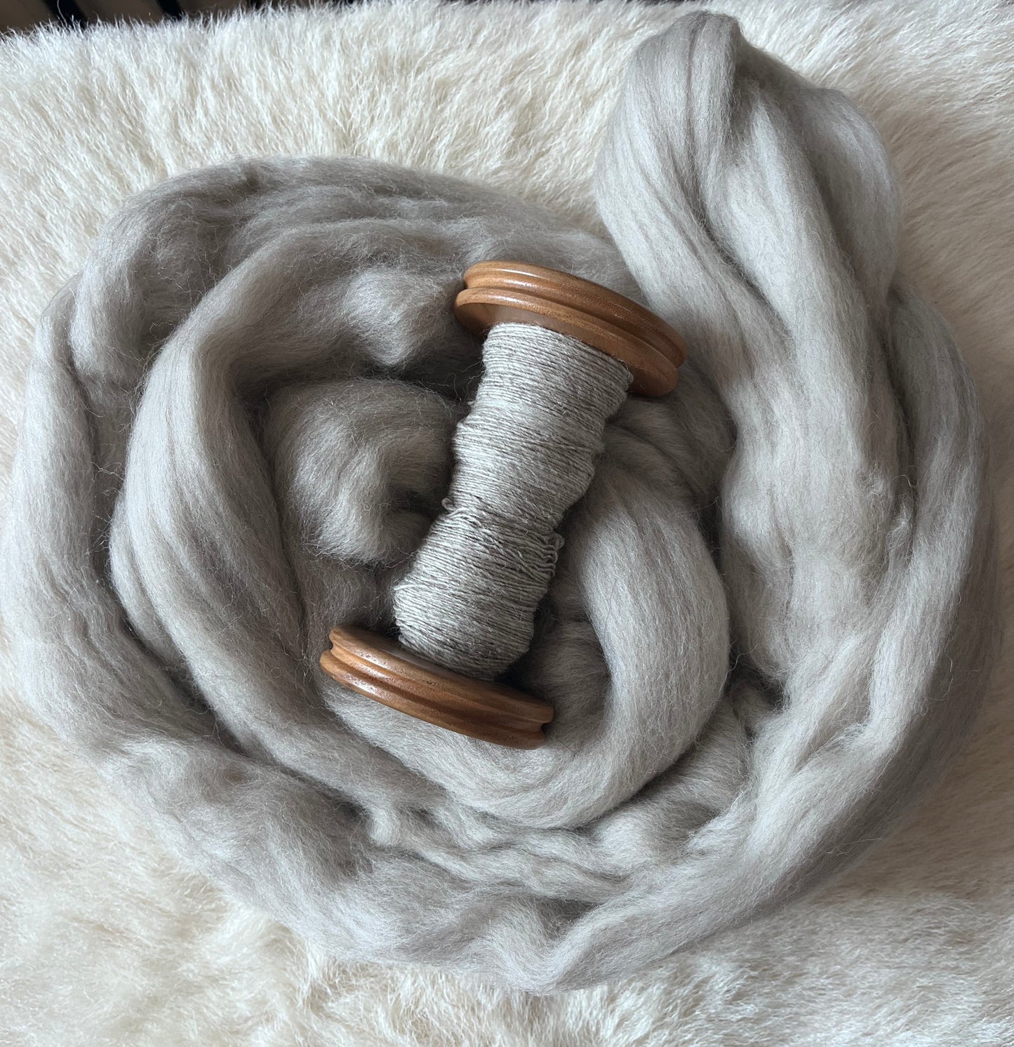 A sample of handspun light grey Polwarth wool fiber on a wooden bobbin