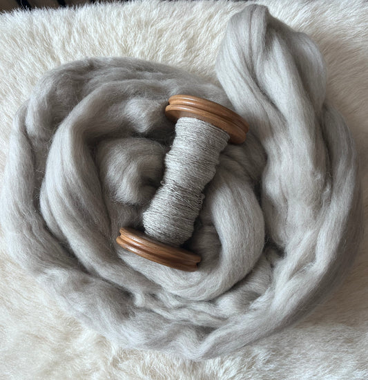 A sample of handspun light grey Polwarth wool fiber on a wooden bobbin