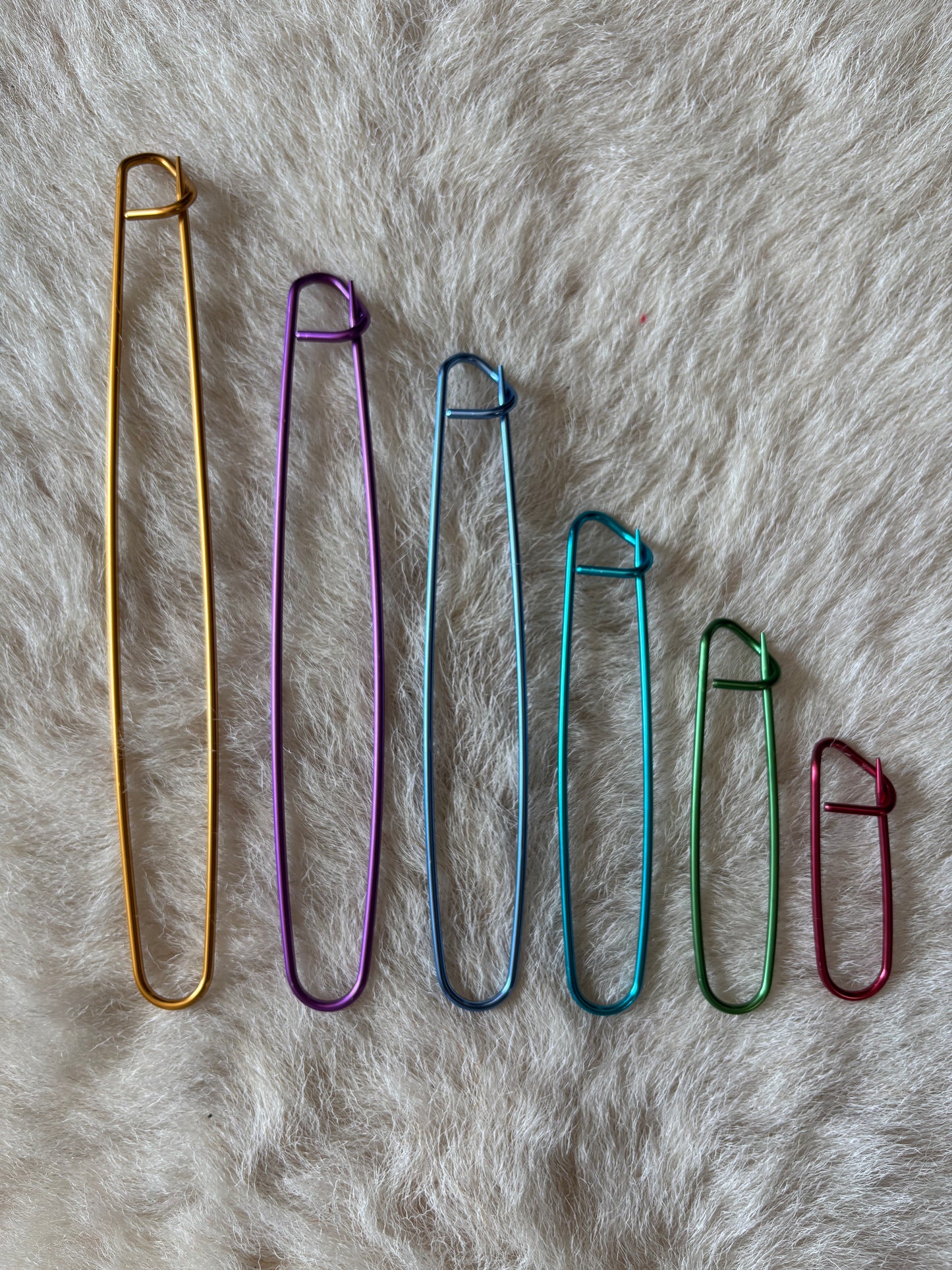Six metal knitting stitch holders in a variety of sizes